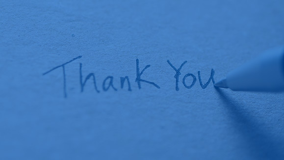 Close-up of the tip of a pen writing “Thank You” on paper.
